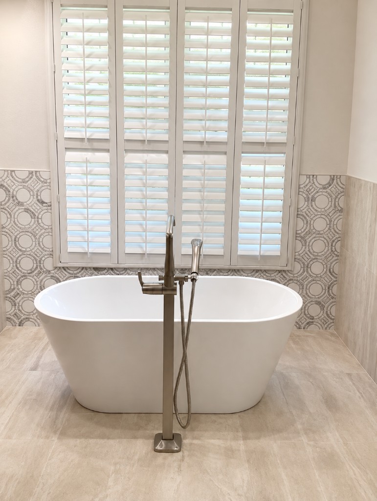 Freestanding soaking tub in front of a circular mosaic feature wall and plantation shutters