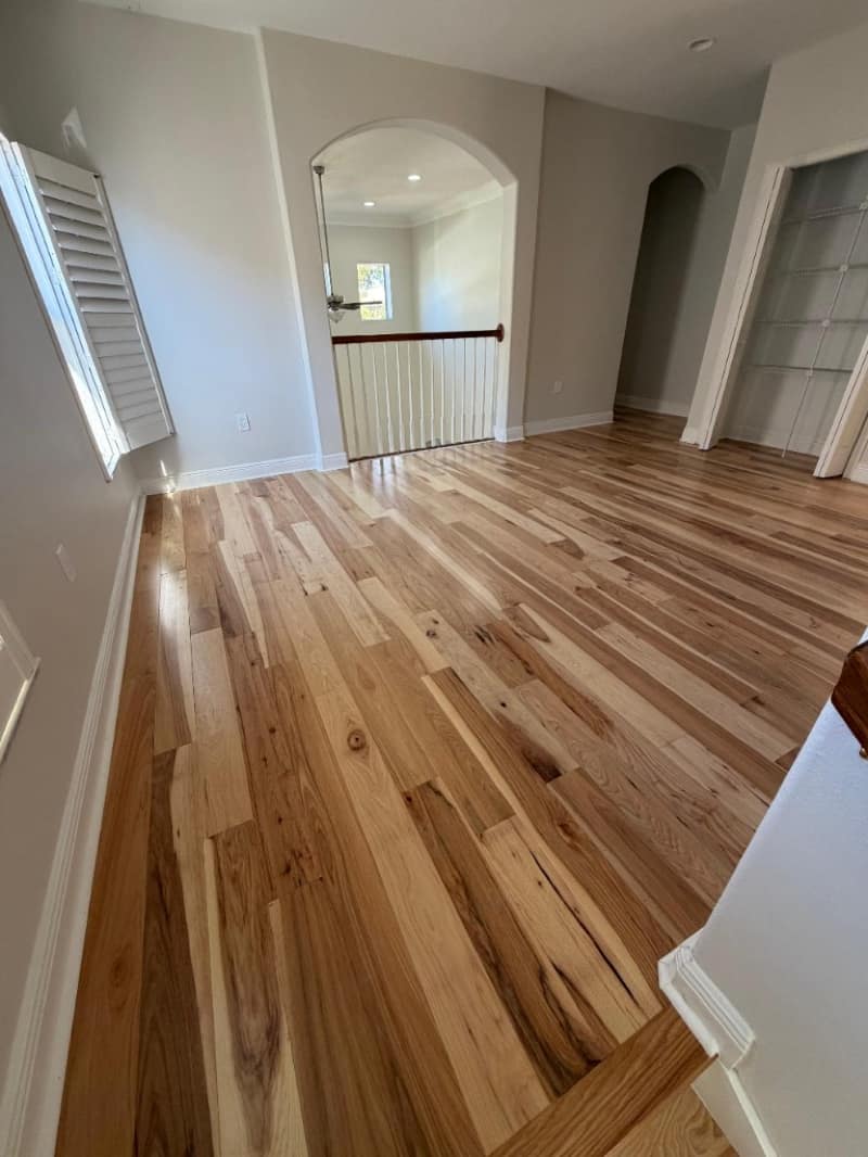 Bright room with character-grade hickory hardwood, white plantation shutters and an arched opening to a stair landing